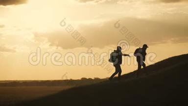 在两个登山者之间帮忙的剪影。 山顶上有两个徒步旅行者，一个人帮助一个人爬上一个纯粹的地方